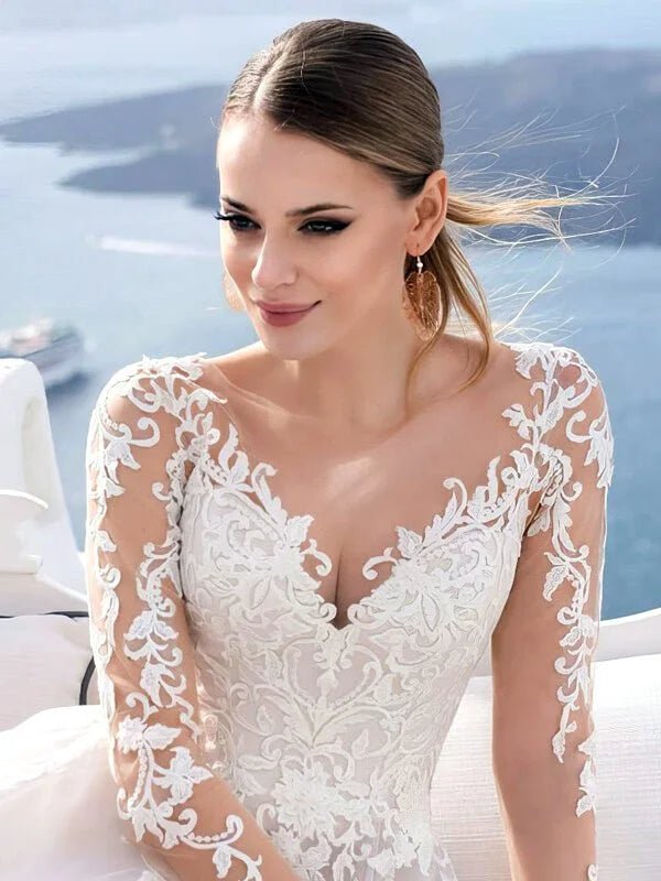 Robe de mariée chic et classe avec bustier en dentelle brodée, décolleté illusion et manches longues transparentes, style élégant et raffiné avec détails floraux.