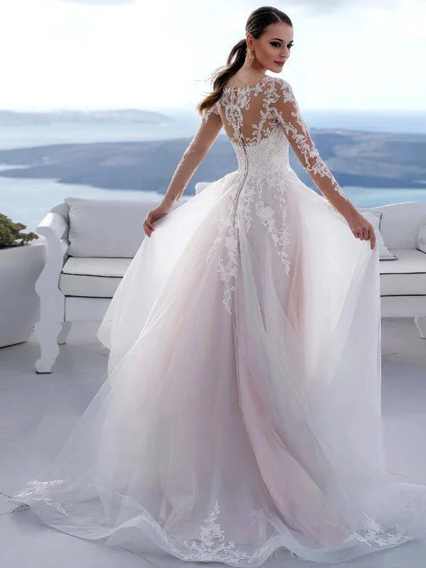 Robe de mariée chic et classe vue dos en dentelle fine avec manches longues transparentes, dos illusion brodé et jupe fluide en tulle ivoire légèrement rosé, traîne élégante.
