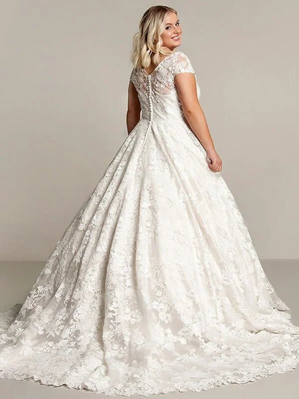Robe de mariée romantique pour femme ronde vue dos en dentelle florale avec manches courtes, coupe princesse et jupe volumineuse avec traîne élégante.