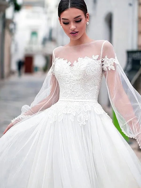 Robe de mariée bohème champêtre en tulle ivoire avec manches longues transparentes, bustier brodé de dentelle florale et jupe fluide volumineuse, style romantique élégant.