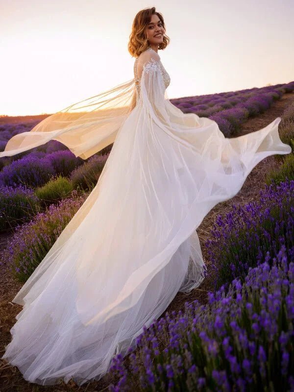 Robe de mariée fluide bohème en tulle léger avec manches longues transparentes et dentelle délicate, silhouette aérienne et romantique.