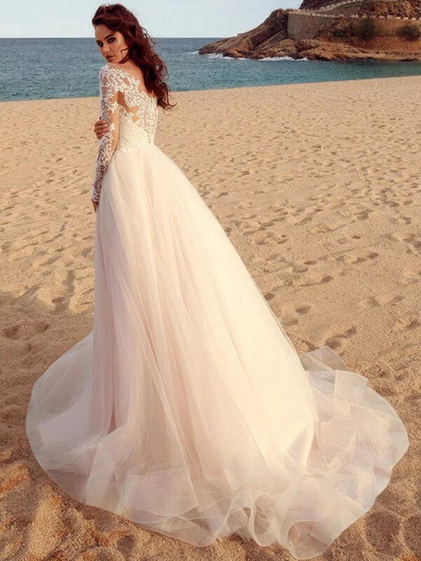 Robe de mariée champêtre en dentelle romantique vue dos, manches longues en transparence, dos travaillé en broderies florales et jupe fluide en tulle ivoire avec traîne légère sur plage.